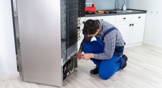 A man in a uniform repairing a fridge